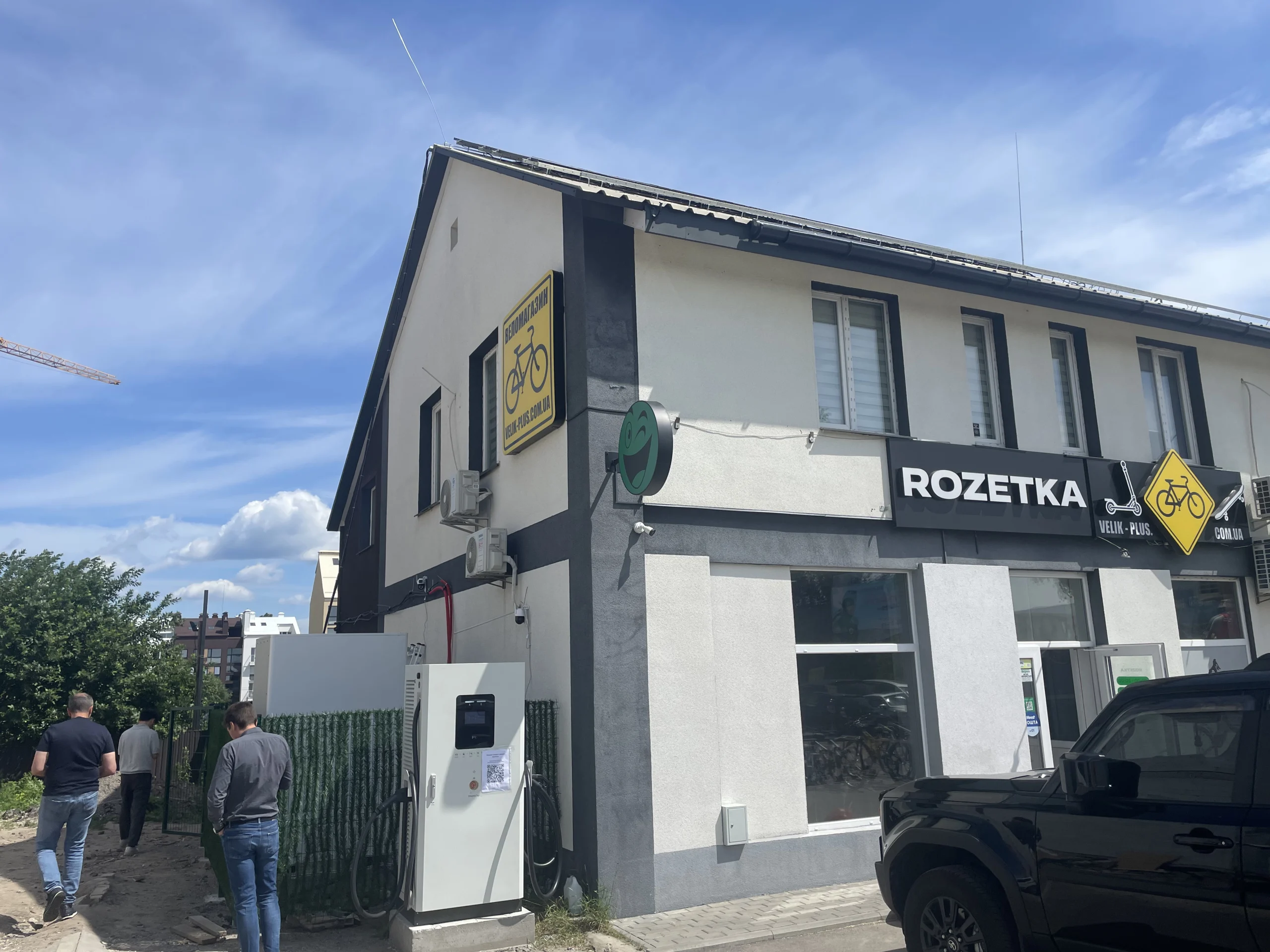 EV töltőállomás telepítése egy ukrajnai projekt helyszínen egy kereskedelmi épület mellett, bemutatva egy 100kW/261kWh napelem-plusz-tárolás töltési elrendezést.
